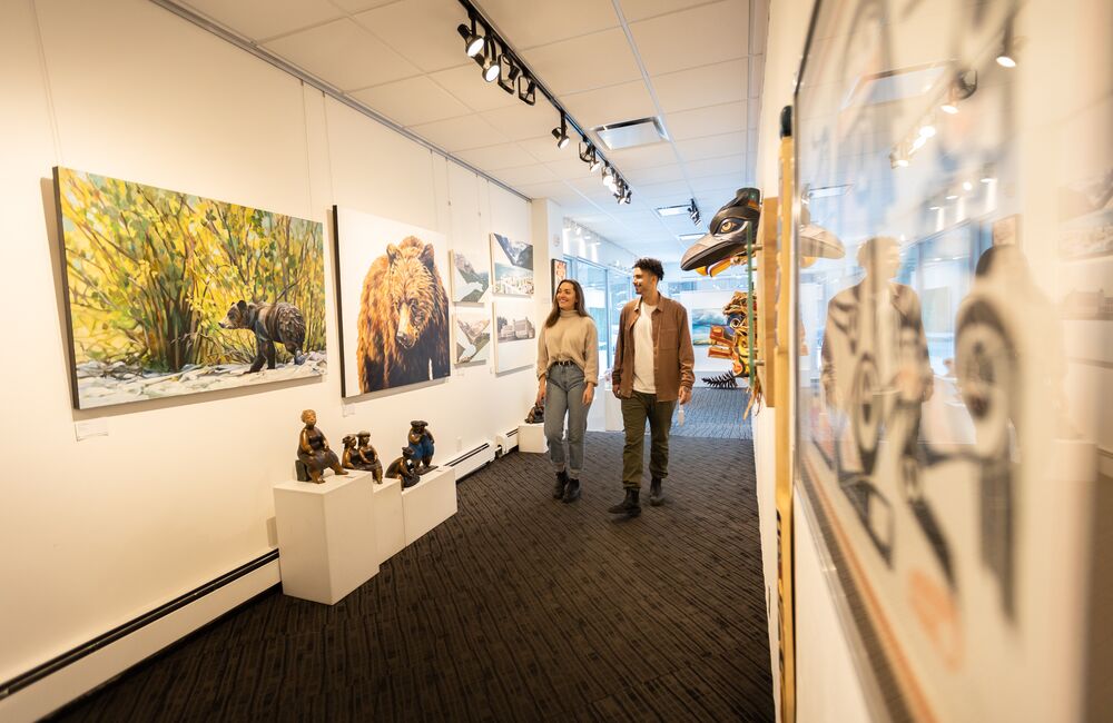 Two people walk through a gallery with art on both sides of bears in Banff National Park.